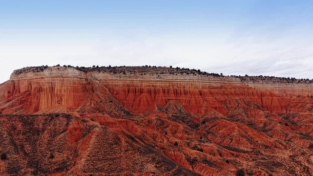 Red clay cliffs and rock formations in Teruel, Aragon, Spain. Wide panoramic view of geological layers under a pale overcast sky with sparse green bushes.