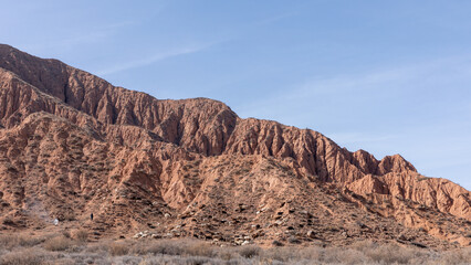 Naklejka premium Wide view of Mars Canyon with red sandstone ridges, dry steppe and grazing livestock under a clear sky, a scenic natural landmark in Kyrgyzstan, Central Asia