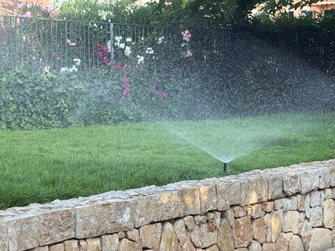 Automatic sprinkler system watering green grass in a residential garden, spraying water droplets across the lawn for efficient irrigation and property landscape care