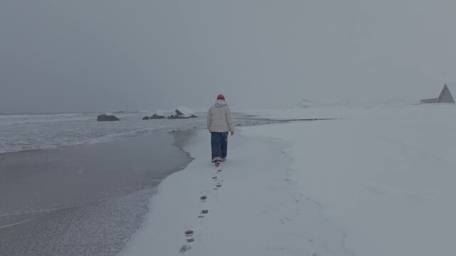 Solitary figure walking along snowy shoreline with footprints