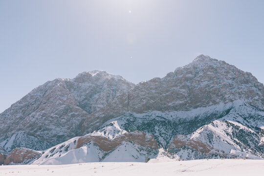 Wide winter landscape with snow-covered rocky mountains and bright sun above the Pamir Highway near Sary-Tash, Osh Region, Kyrgyzstan, with open valley foreground