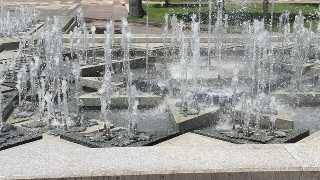 Cascading Water Feature: A modern water fountain with multiple tiers and jets of water creates a dynamic display, set against an outdoor urban backdrop.