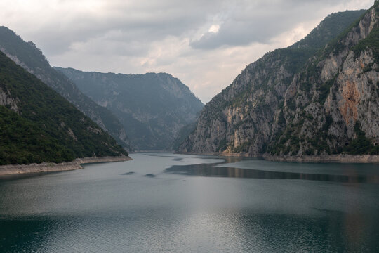 Wide view of Piva Lake framed by steep rocky mountains and forested slopes under overcast sky, near Pluzine, Savnik Municipality, Montenegro