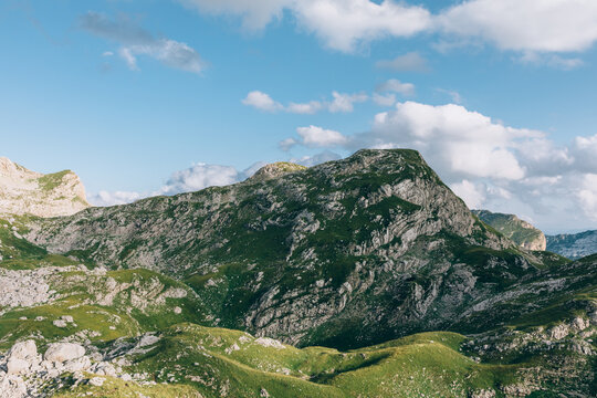 Scenic rocky mountains and green alpine meadows on the hiking route to Bobotov Kuk in Durmitor National Park, Montenegro, under blue sky with clouds