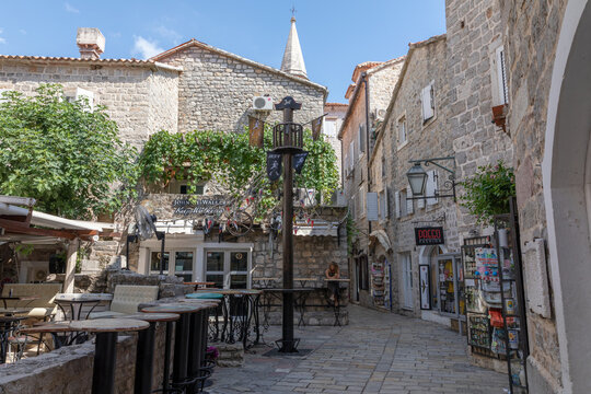 Budva, Montenegro - August 3, 2025: Sunny pedestrian lane with stone houses, outdoor cafe tables and small shops in Budva Old Town, Budva, Montenegro, popular Adriatic travel destination