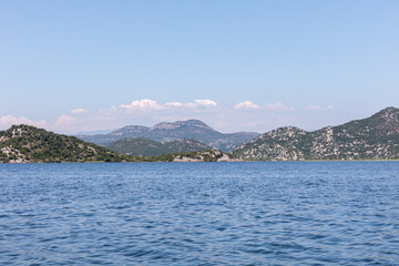 Fototapeta premium Wide landscape of Skadar Lake with calm blue water, green rocky hills and distant mountains under clear sky, near Virpazar, Montenegro, summer travel nature scene