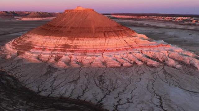 Aerial view of Mount Bokty featuring unique layered geological formations and arid desert landscape during sunset in Karakiya District, Mangystau Region, Kazakhstan.