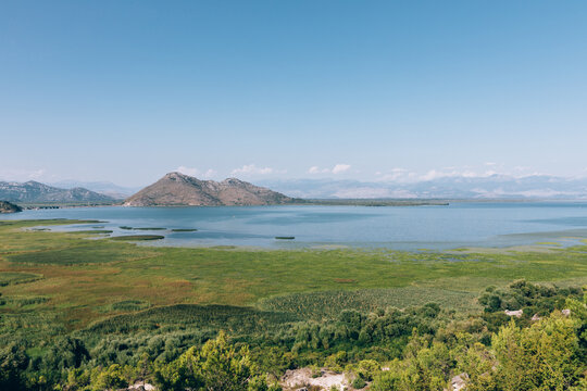 Wide panoramic landscape of Skadar Lake with green wetlands, calm water and distant mountains on a sunny day, Montenegro, a popular nature reserve and travel destination