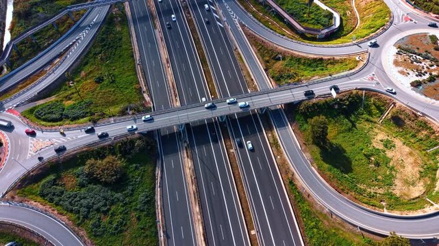 Top down perspective of a highway overpass bridge, Spain. Direct vertical view of multiple lanes, moving traffic, white cars and green roadside vegetation.
