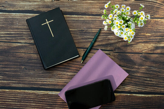 Holy Bible with Cross, Smartphone and Notebook on Wooden Table. Christian faith, Bible study, prayer journaling, devotion, worship, spiritual growth, and modern Christian lifestyle concept.