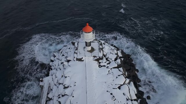 Small White Lighthouse with Orange Roof on Snowy Rocky Jetty in Winter Sea