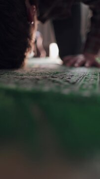 Muslim man performing prostration Sujood on a green prayer rug at home, bowing down in prayer.
