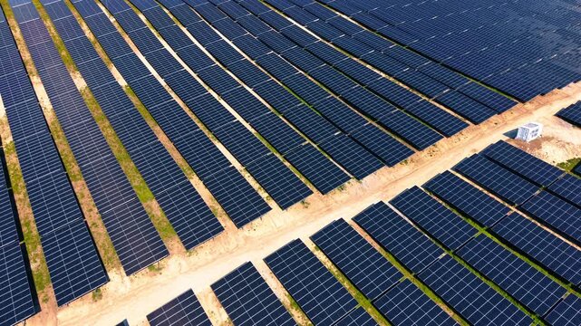Overhead view of solar panel grid with maintenance road intersection. Top down drone shot of dark photovoltaic rows, sandy pathways, and transformer station in warm light.