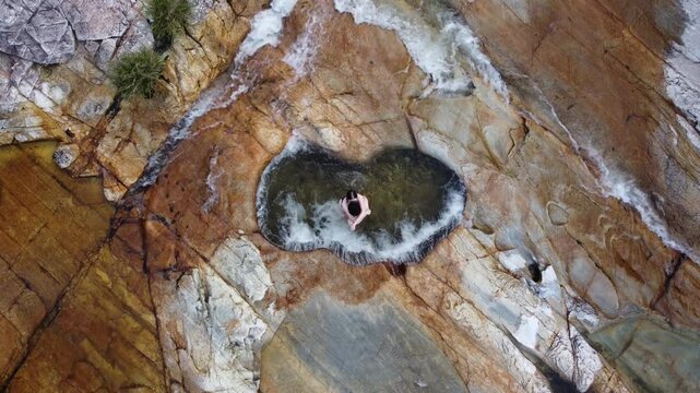 Couple embracing and kissing in the heart-shaped natural pool at Capivara Waterfall, Serra da Canastra, Brazil, filmed by drone above crystal-clear waters and surrounded by pristine nature.