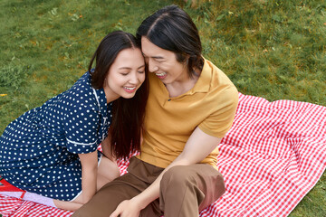 Naklejka premium Young couple enjoys a joyful moment together on a vibrant picnic blanket in the park