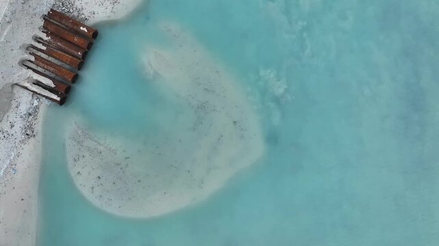 Aerial view of rusty industrial pipes discharging into turquoise water along a sandy shoreline in Gulhi, Kaafu Atoll, Maldives.