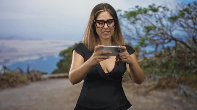 Young blonde woman holding smartphone and tapping screen, visible cleavage, wearing glasses in studio; mobile gaming focus.