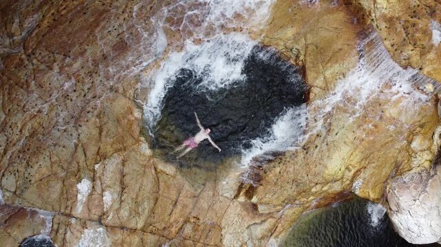 Drone footage of a man relaxing in a crystal-clear natural pool at Capivara Waterfall, Serra da Canastra, Brazil, as the camera pulls back to reveal the entire landscape and pristine waters.