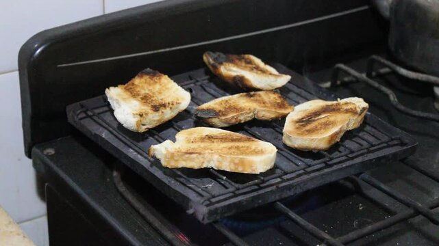 Tostadas en el tostador de metal r&uacute;stico huneando al tostarse, el contraste de las tostadas con el quemador con fuego azul crea una atm&oacute;sfera hogare&ntilde;a.