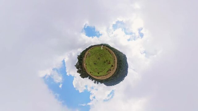 Happy latina woman dancing, expressing joy and freedom on a grassy hill in a tiny planet drone shot
