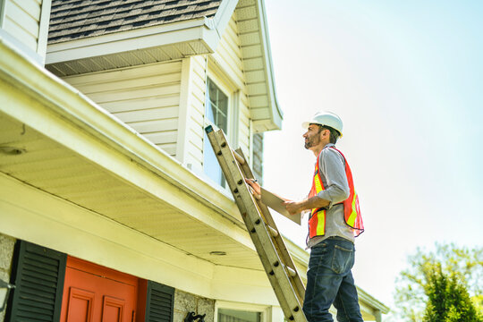Man with a white hard hat holding a clipboard, inspect house
