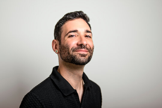 Young man with beard in casual attire with suspenders poses confidently by wall