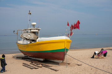 Naklejka premium Fishing boat on shore, people, beach, April. Sopot, Poland.