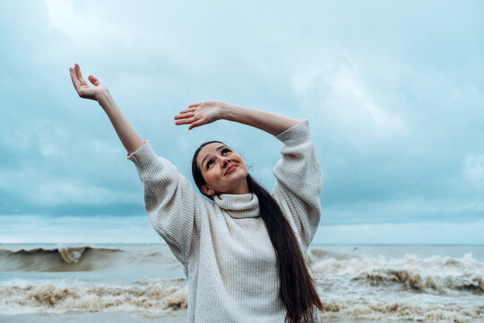 Woman dancing by the stormy sea wearing a sweater