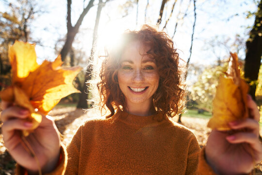 Happy redhead woman holding maple leaves at autumn park