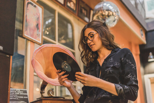 Portrait of smiling young woman standing in front of antique shop looking at gramophone record