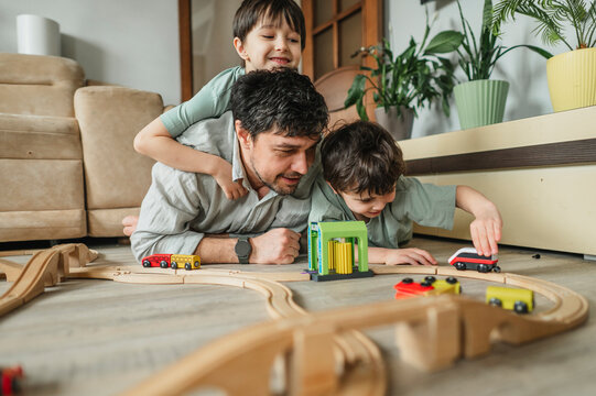 Father and sons playing with wooden train at home