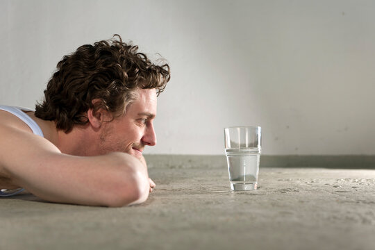Mid adult man lying on floor and staring at glass of water