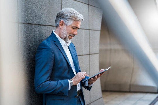 Mature businessman standing at a wall using tablet