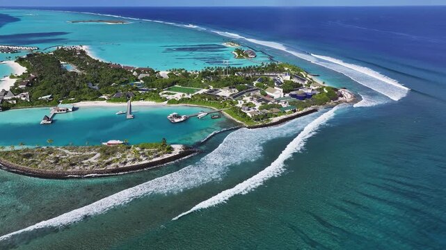 Aerial view of a resort island featuring turquoise lagoons, white sand beaches, and waves breaking over the coral reef in Thulusdhoo, Kaafu Atoll, Maldives.