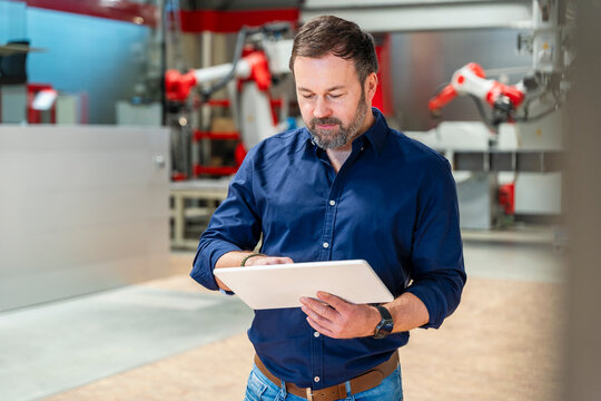 Factory manager using tablet with industrial robot indoors
