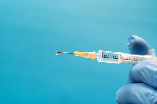 Hand of person wearing protective glove holding single syringe