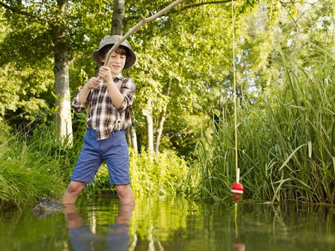 Boy wading and fishing with a wooden rod in a stream