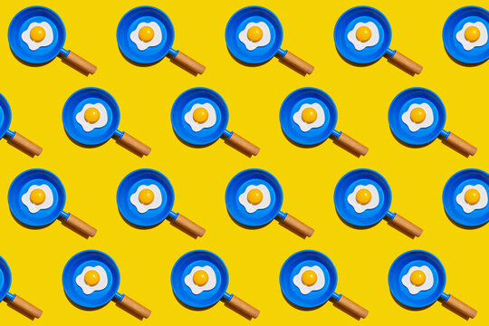 Pattern of rows of fried eggs on blue pans against yellow background