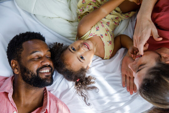 Happy daughter lying down with parents on bed at home