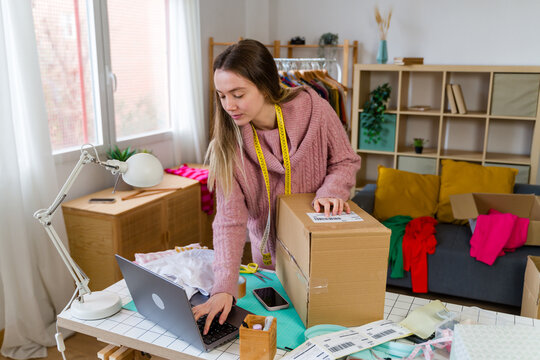 Entrepreneur typing on laptop and packing shipping box in home office