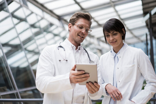 Doctor's standing in atrium, using digital tablet, discussing solutions