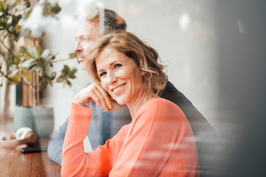 Smiling woman sitting in front of man at cafe seen through glass