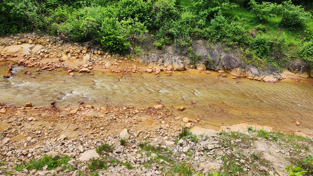 A stream colored red-orange by mining pollution, showing acid mine drainage effects where dissolved metals oxidize and form iron-rich sediments in the water and riverbed.
