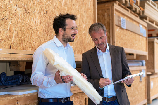 Happy businessman holding insulation with colleague signing contract at warehouse