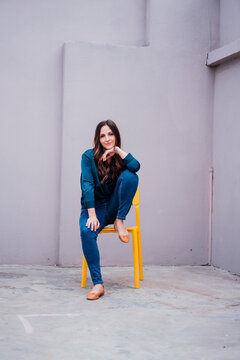 Young woman sitting on yellow chair in front of wall