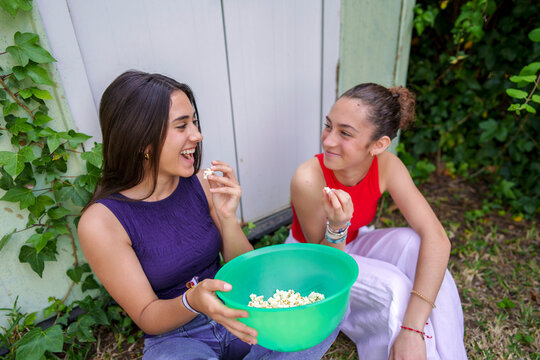 Girlfriends enjoying popcorn from a bowl and smiling in the garden outdoors