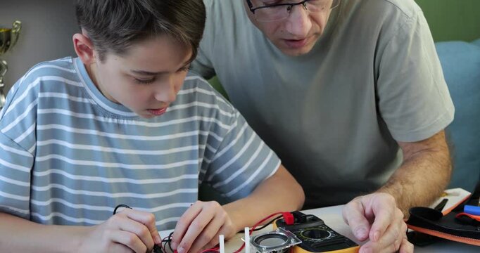 Father and son work together on electronics project at home. Boy learns practical technology skills through hands-on STEM education, mentorship and shared learning experience