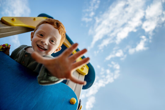 Smiling boy on playing equipment showing palm under sky