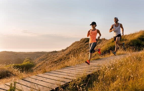 Spain, Aviles, athletes couple running along a coastal path at sunset
