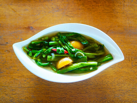 ⁠A top-down view of Indonesian style stir-fried yellow velvetleaf vegetables, known as tumis genjer, served with chili in a white leaf-shaped bowl